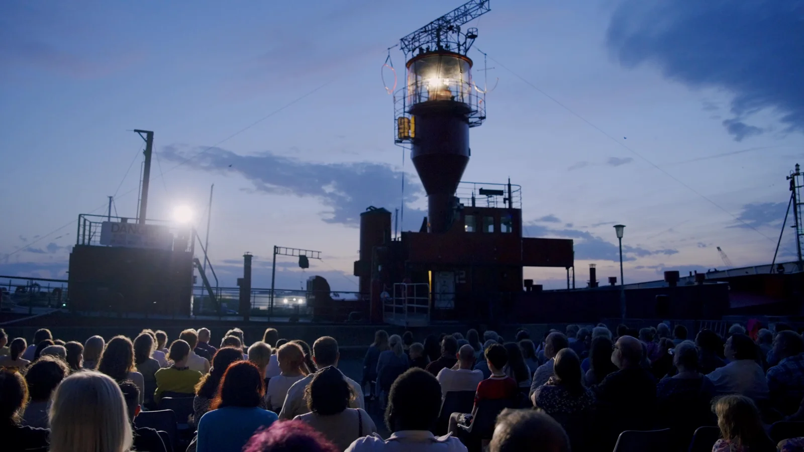 The audience gathered on the wharf beneath the lightship at dusk