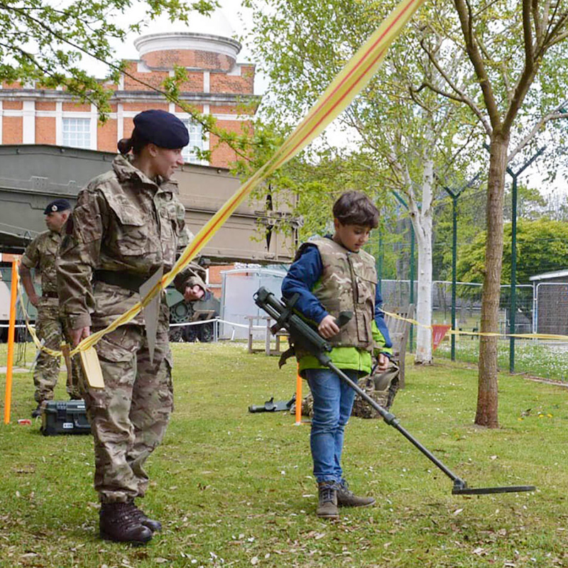 A soldier and a young visitor using a metal detector outside the museum